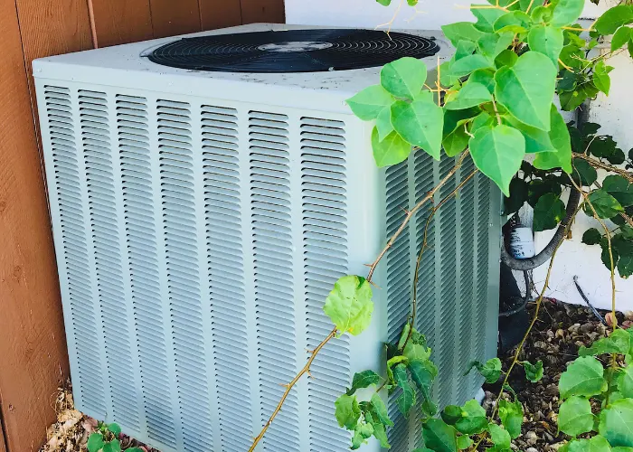 An HVAC unit in great condition by a brown wooden fence and a vine